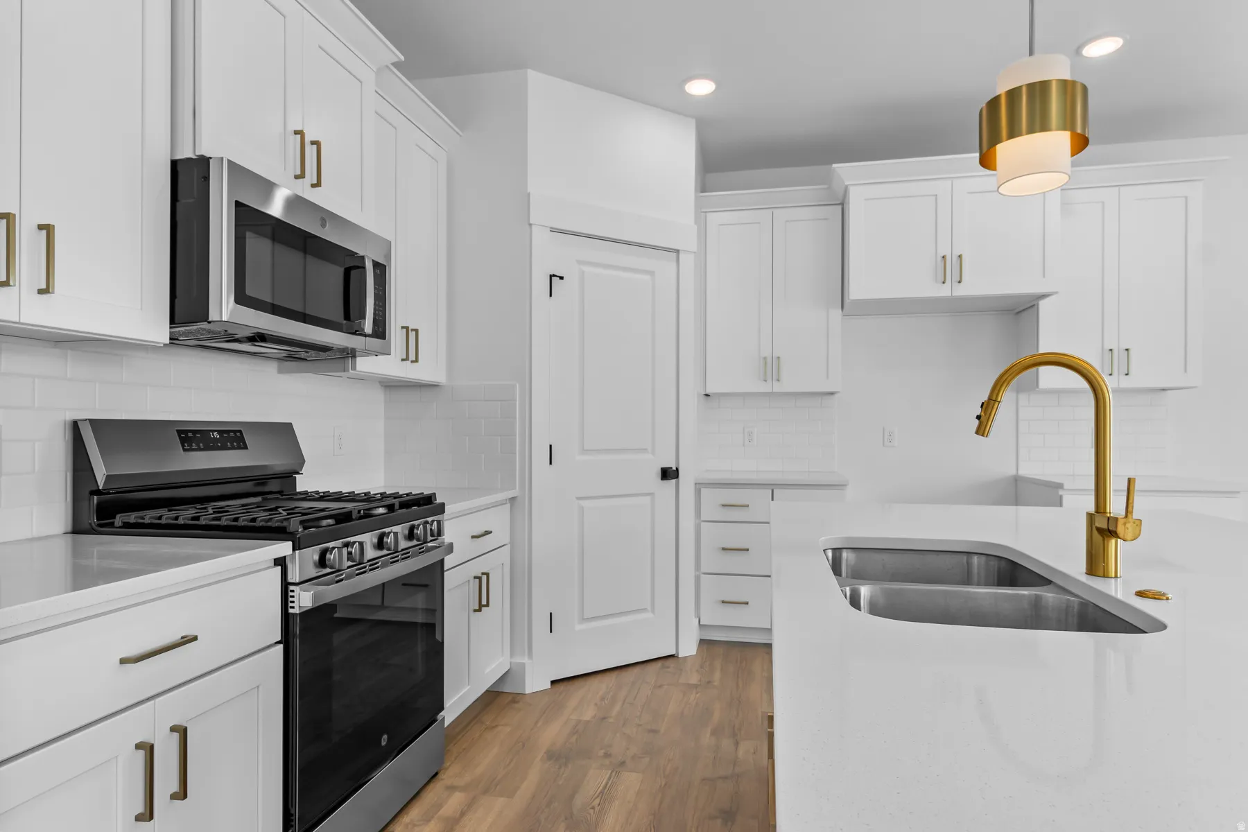 Modern kitchen featuring white shaker-style cabinetry with brushed brass hardware, stainless steel gas range with six burners, and a matching over-the-range microwave
