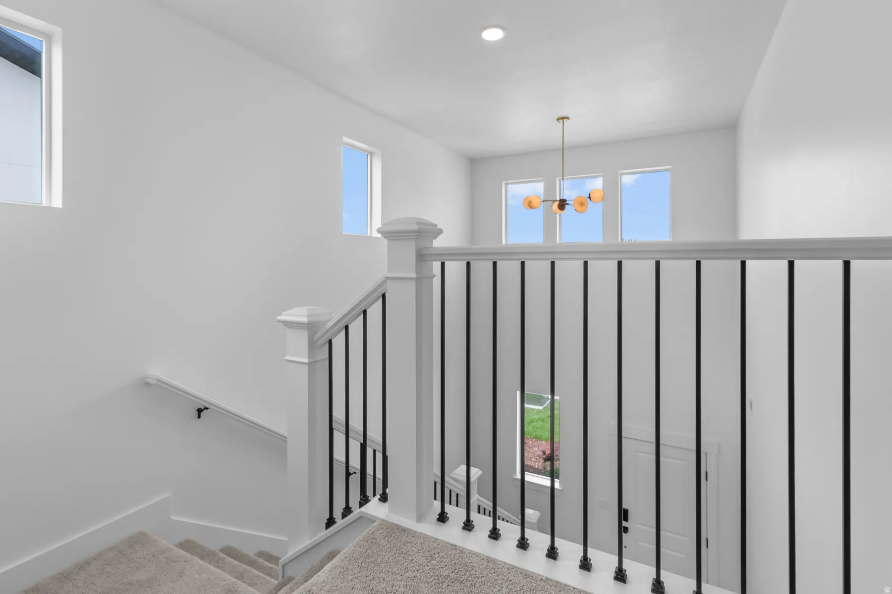 Elegant upper-level landing featuring a modern black metal railing with vertical balusters, recessed ceiling lighting, and multiple windows flooding the space with natural light