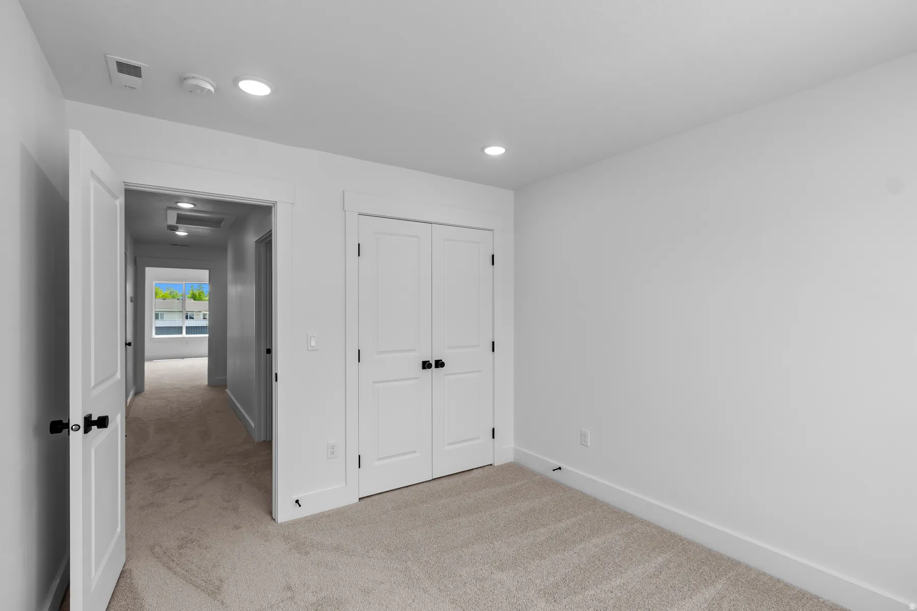 Spacious bedroom featuring neutral wall finishes, recessed ceiling lighting, and double closet doors with black hardware