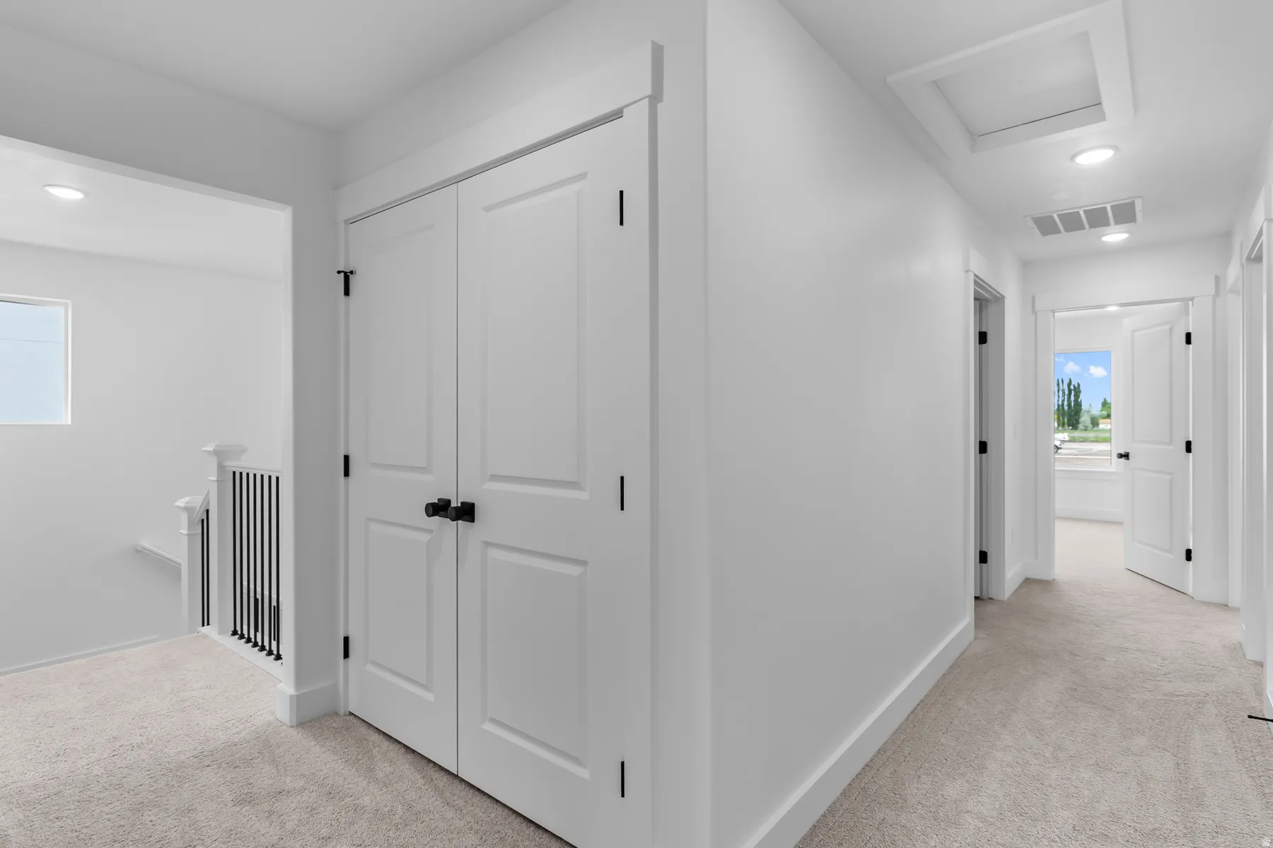 Bright hallway featuring pristine white drywall, recessed ceiling lighting, and neutral carpeting