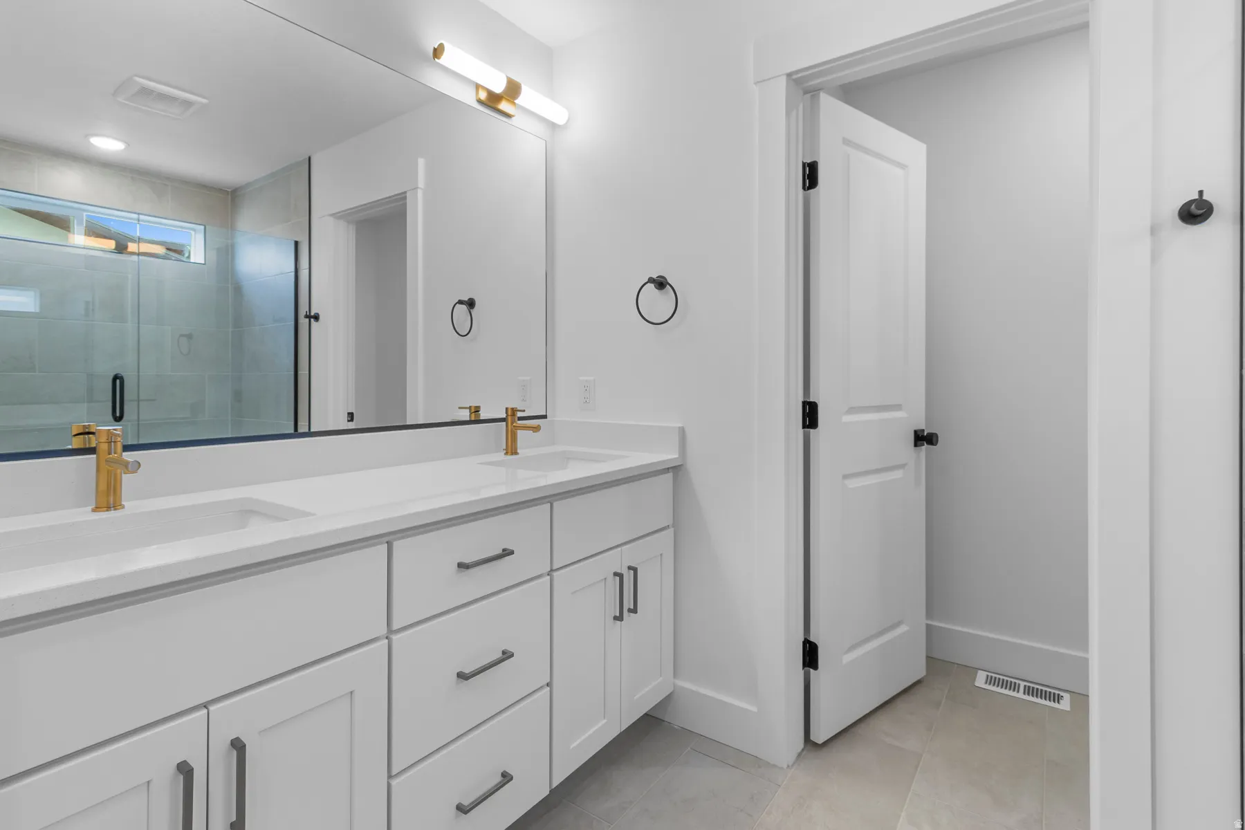 Spa-inspired primary bathroom featuring a double-sink vanity with white cabinetry, brushed gold hardware, and a quartz countertop