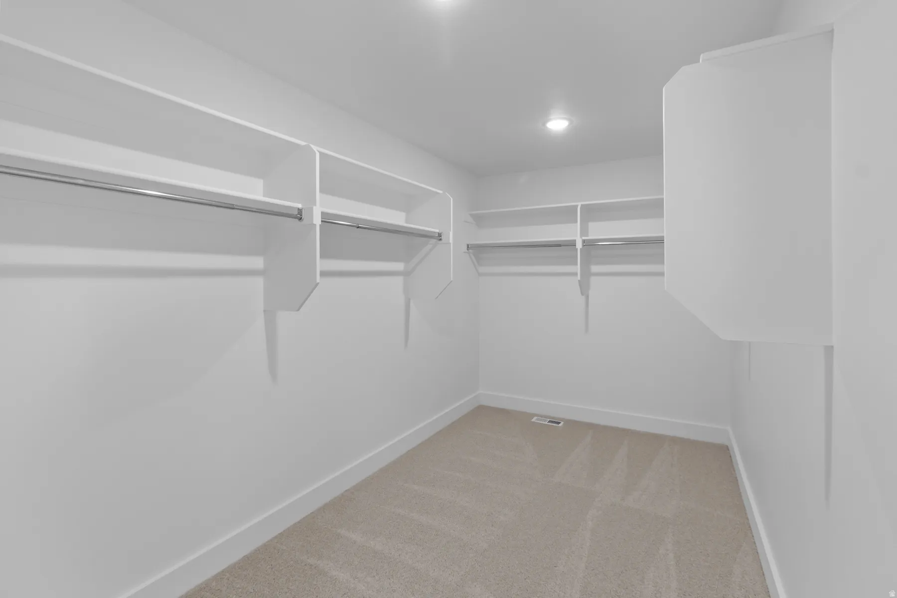 Spacious walk-in closet featuring white built-in shelving and hanging rods throughout, wood-finish flooring, and recessed lighting for optimal visibility and organization