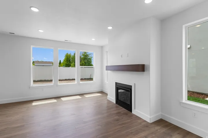 Bright, open living space showcasing gleaming wood-finish flooring, recessed ceiling lighting, and abundant natural light from triple casement windows