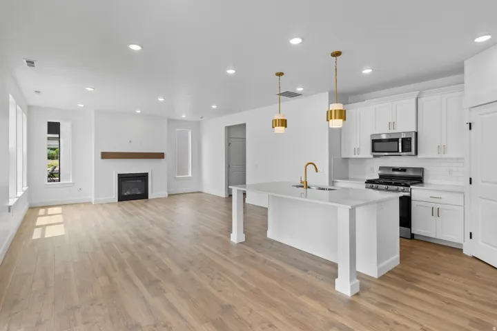 Open-concept kitchen and living area featuring white cabinetry, stainless steel appliances, and a large island with waterfall-edge countertop