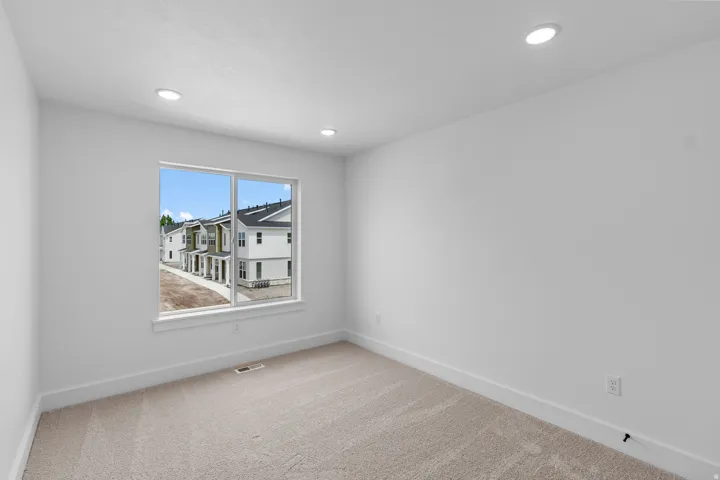 Bright secondary bedroom featuring large dual-pane windows with expansive natural light, neutral wall finishes, carpet flooring, and recessed ceiling lighting