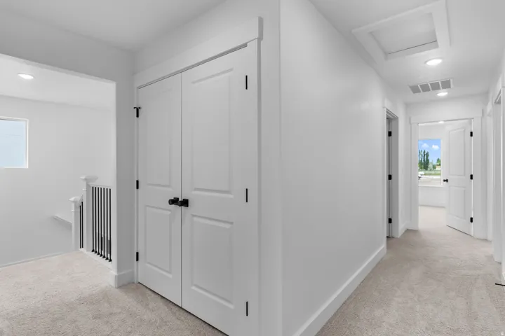 Bright hallway featuring pristine white drywall, recessed ceiling lighting, and neutral carpeting