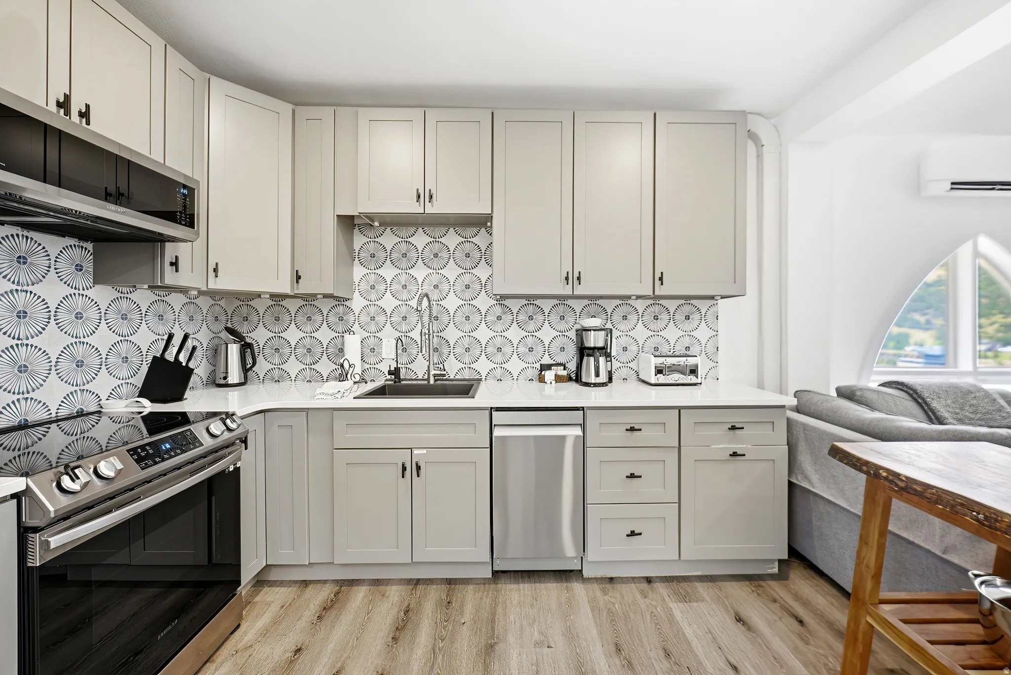 Modern kitchen featuring light gray cabinetry, stainless steel appliances, a patterned tile backsplash, and wood-finish flooring