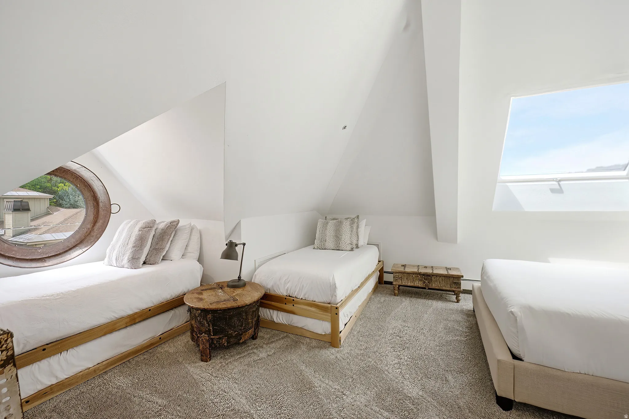 Attic space featuring vaulted ceilings, a porthole window, a large skylight, and gray patterned carpeting
