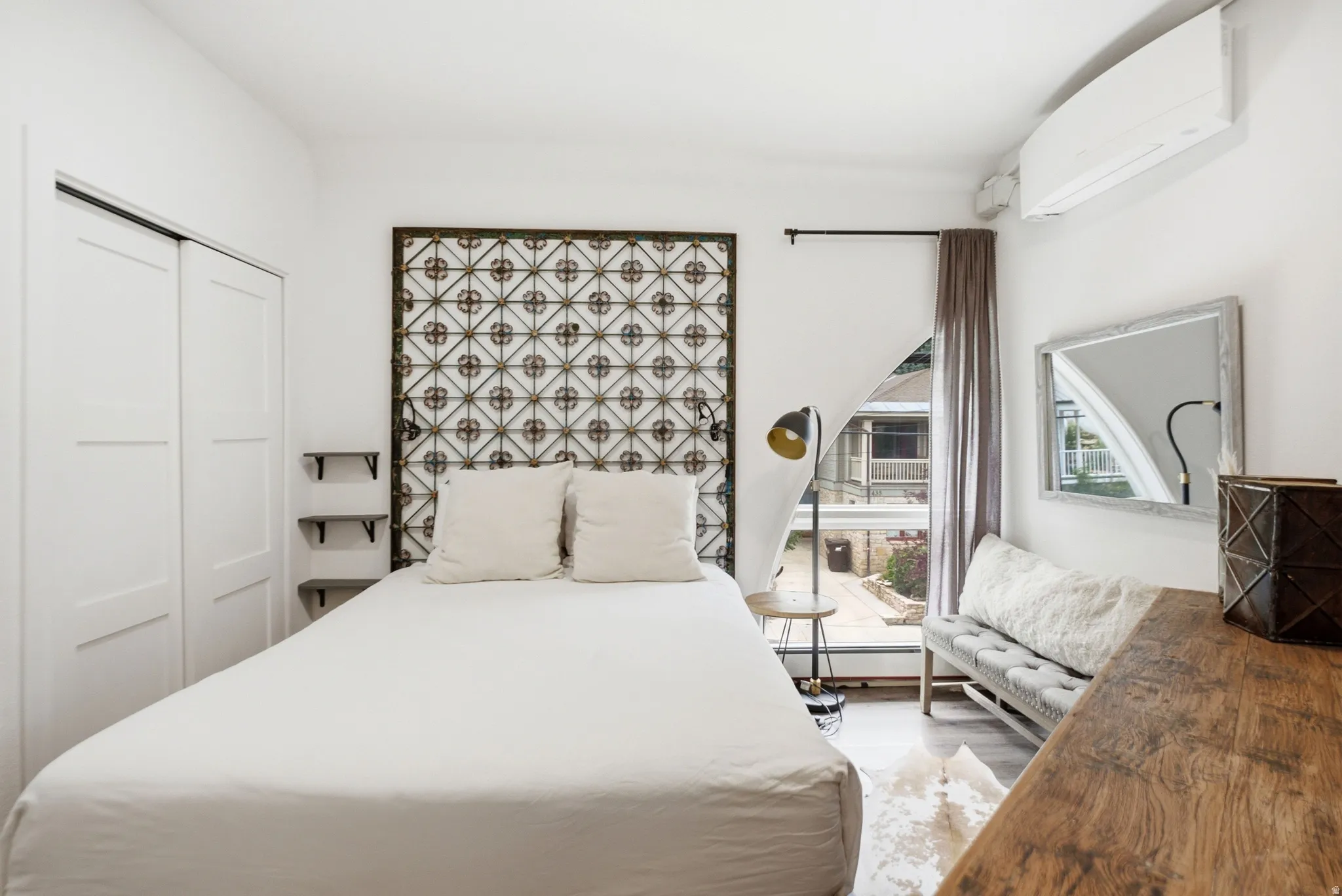 Spacious room featuring light wood-finish flooring, white walls, and a large window with courtyard visibility
