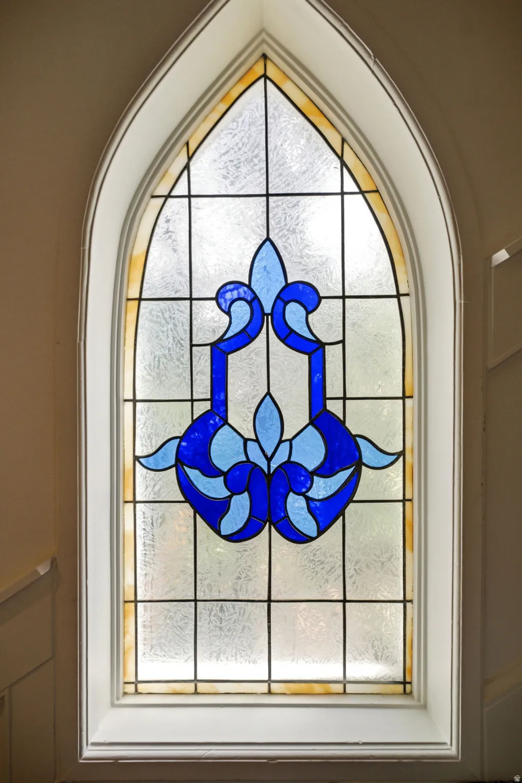 Arched stained glass window featuring blue and light blue design elements, textured glass panes, white trim, and a decorative border