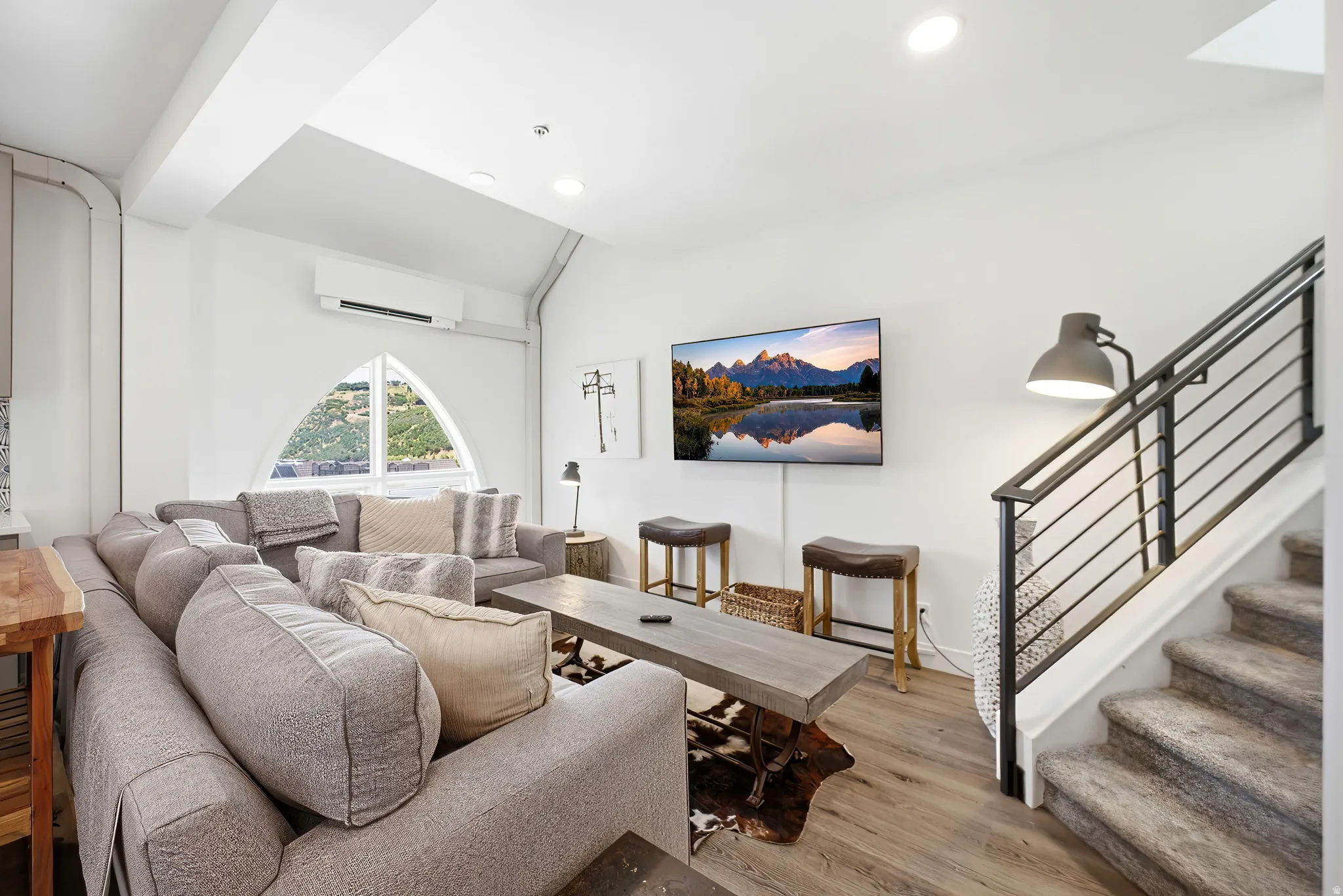 Vaulted ceiling featuring a distinctive arched window, wood-finish flooring, and a modern metal-railed staircase