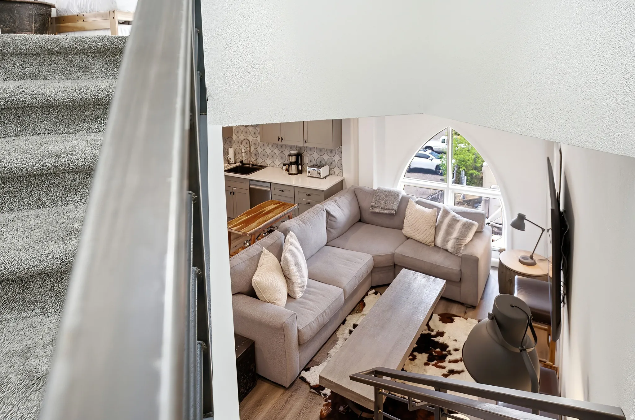 Open-concept living space featuring wood-finish flooring, a contemporary kitchen with light gray cabinetry and a patterned tile backsplash, and an arched window