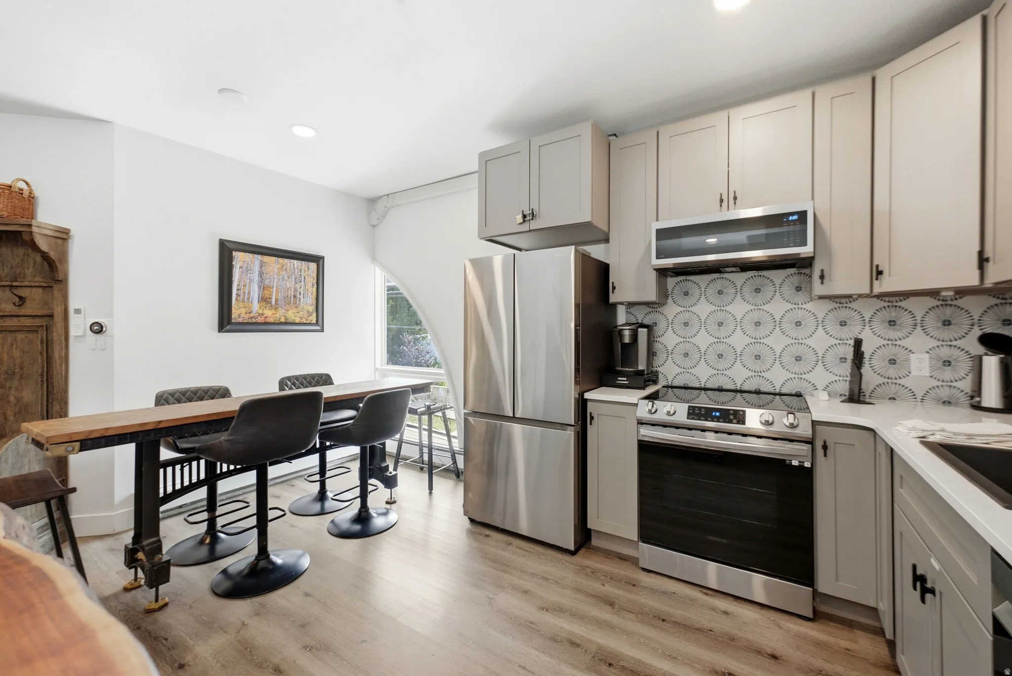 Modern kitchen featuring light-toned cabinetry, stainless steel appliances, patterned tile backsplash, and light wood-finish flooring
