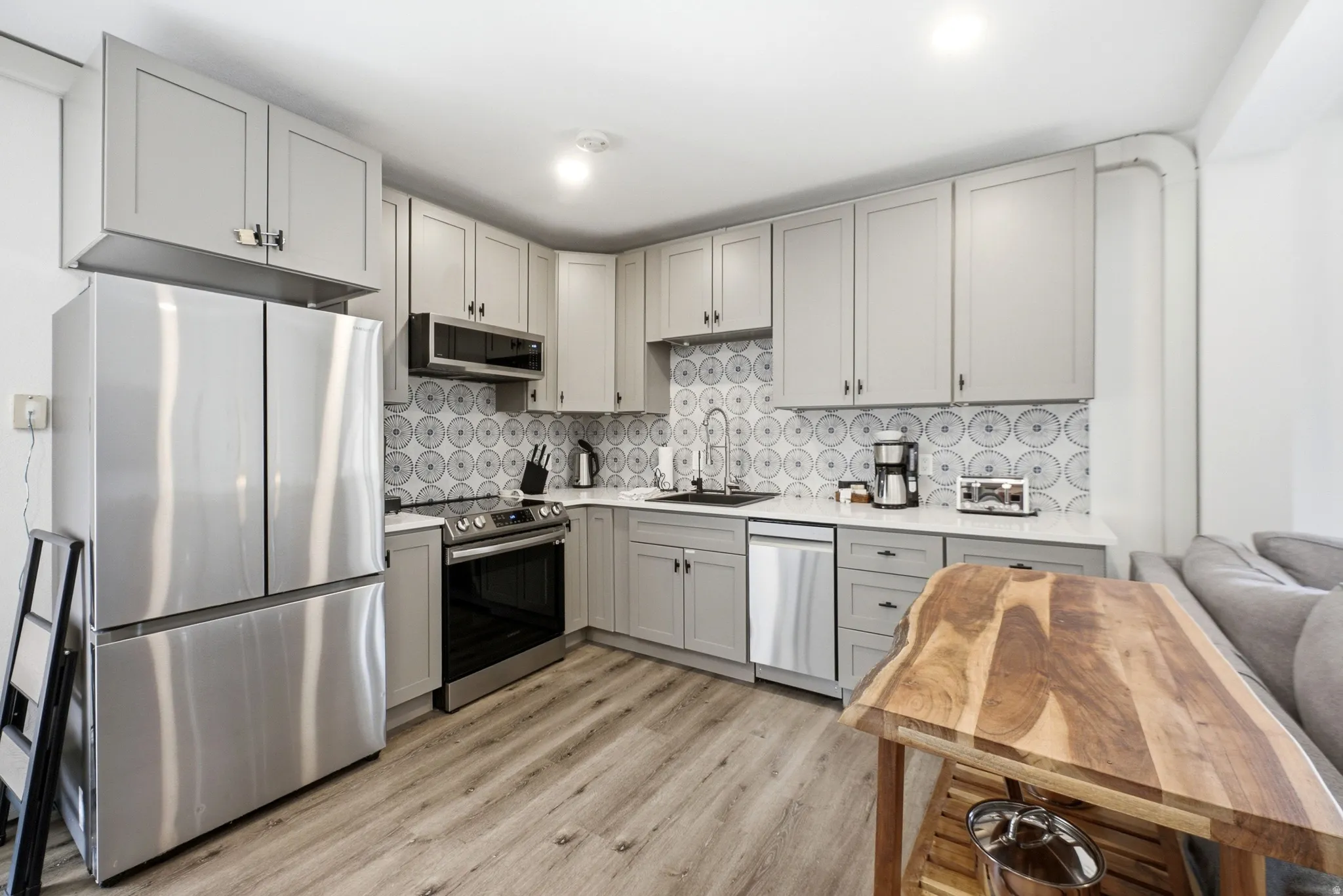 Kitchen featuring light gray cabinetry, stainless steel appliances, patterned tile backsplash, white countertops, and wood-finish flooring