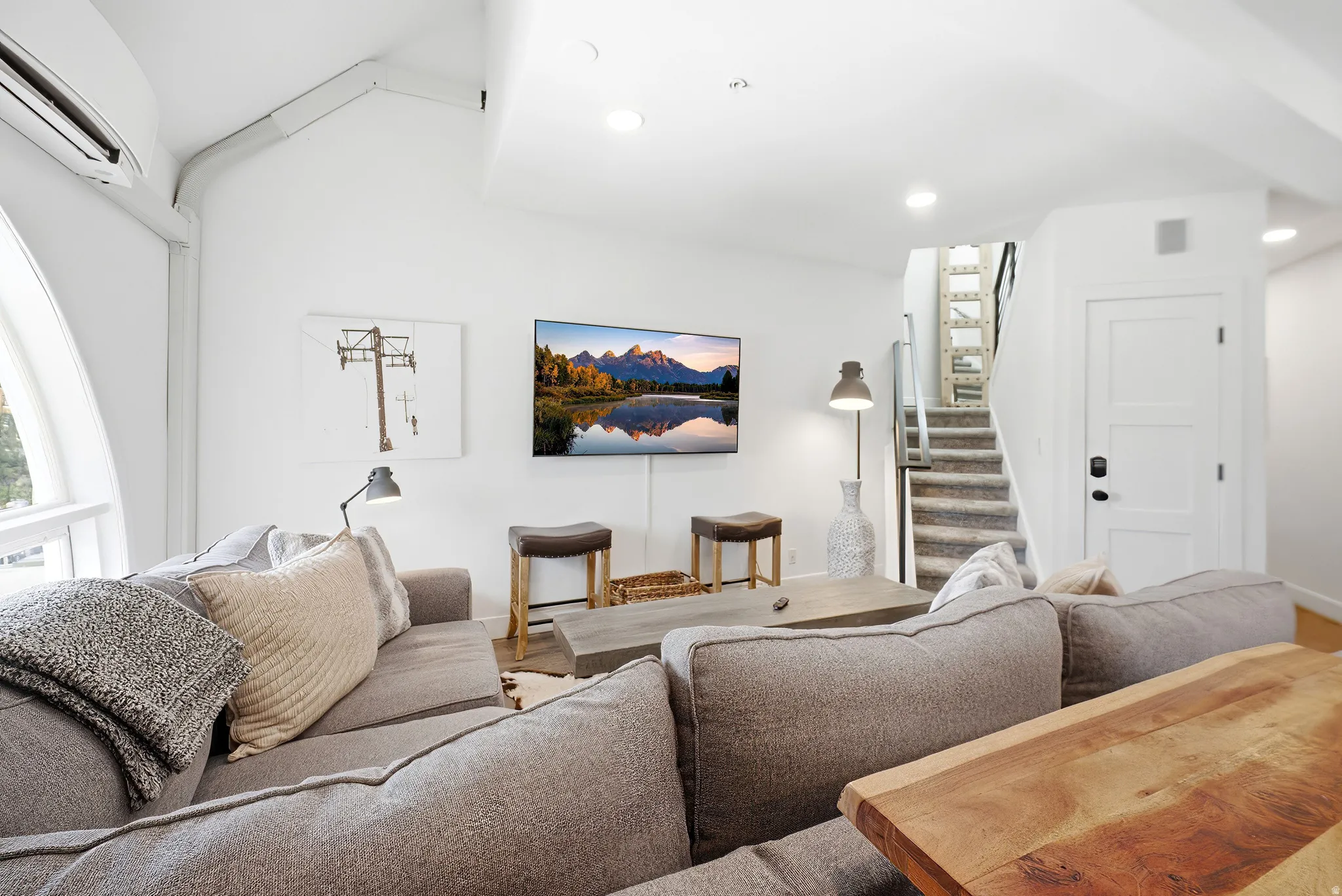 Vaulted ceiling living space featuring a unique arched window, a built-in air conditioning unit, recessed lighting, and a staircase with metal railings