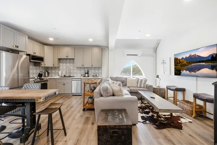Open-concept living area with wood-finish flooring, a kitchen featuring stainless steel appliances and light gray cabinetry, an arched window, and recessed lighting