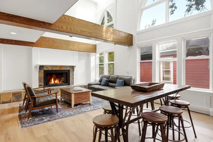 Vaulted great room with exposed wood beams, a stone-clad fireplace, and expansive arched windows