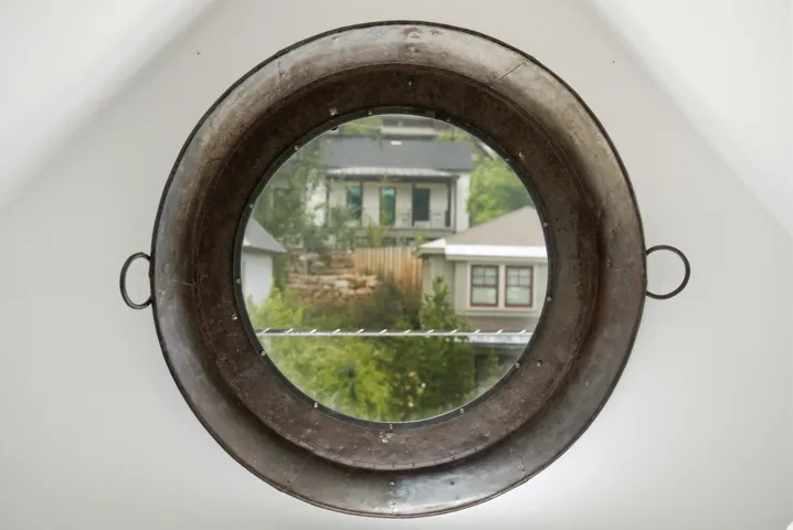 Circular window with a distressed metallic frame and riveted detailing