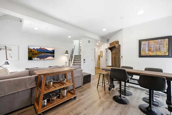 Open-concept living space featuring wood-finish flooring, recessed lighting, and a prominent wood dining table with industrial-style legs