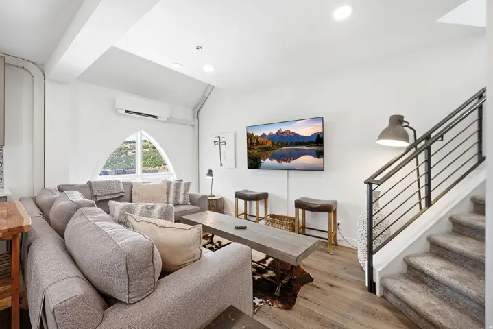 Vaulted ceiling featuring a distinctive arched window, wood-finish flooring, and a modern metal-railed staircase