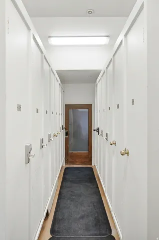 Hallway featuring multiple white storage lockers with various door handles, recessed lighting, and a wood-finish floor