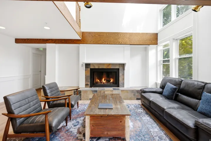 Living area featuring a stone-clad fireplace, soaring ceilings, exposed wood beams, large windows, and hardwood flooring