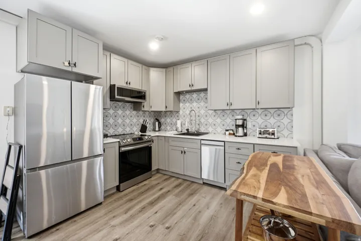 Kitchen featuring light gray cabinetry, stainless steel appliances, patterned tile backsplash, white countertops, and wood-finish flooring