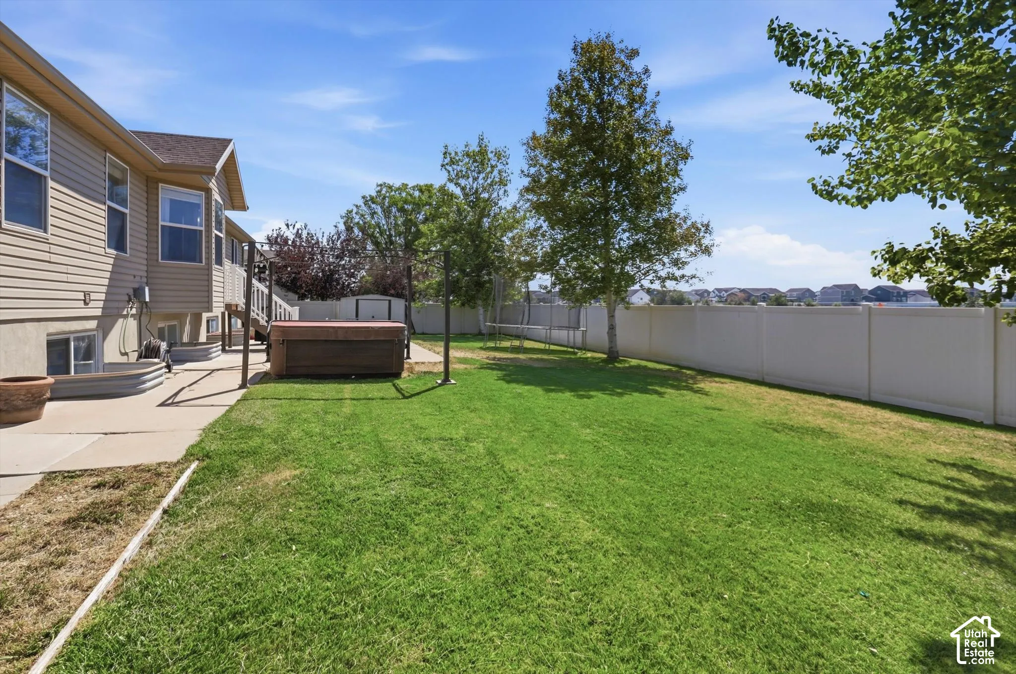 Expansive green lawn framed by a privacy fence, concrete patio, and a hot tub