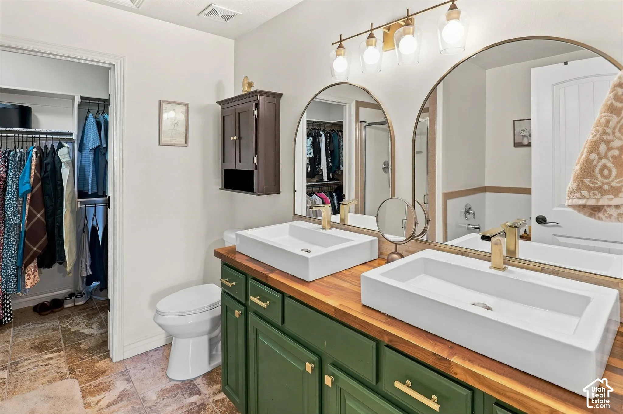 Dual vessel sinks with gold fixtures set on a wood-finish countertop, complemented by green cabinetry and arched mirrors