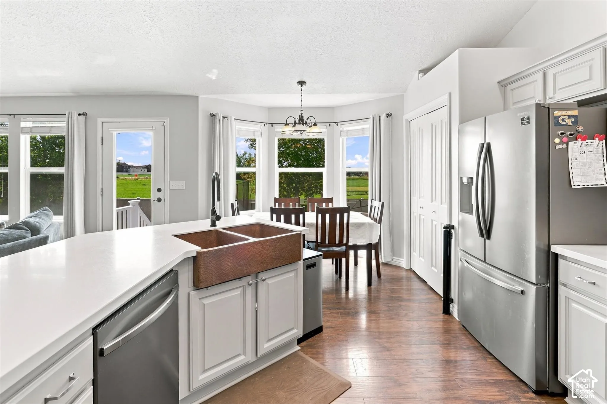 Bright, open kitchen featuring white cabinetry, stainless steel appliances including a French-door refrigerator, and copper farmhouse sink
