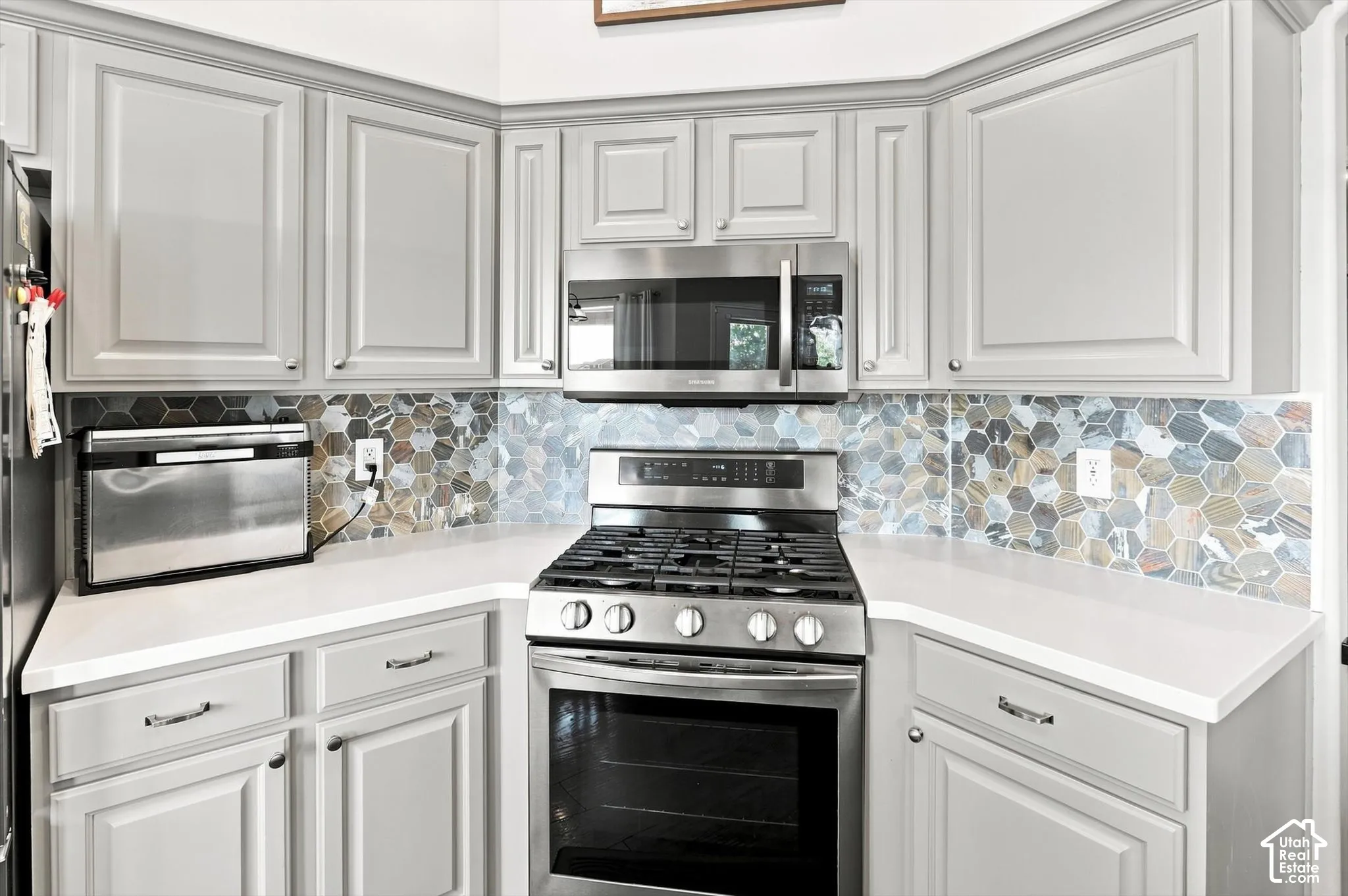 Light gray cabinetry, backsplash and gas stove with microwave