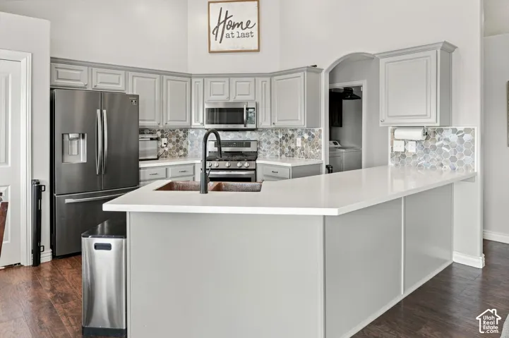 Stunning chef's kitchen featuring light gray cabinetry, stainless steel appliances including a French-door refrigerator and gas range, solid surface countertop,  mosaic tile backsplash, bar