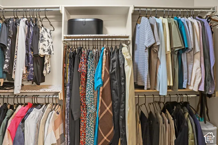 Spacious walk-in closet featuring multiple hanging rods across three sections, wire shelving with integrated storage bin, and abundant capacity for a comprehensive wardrobe organization system