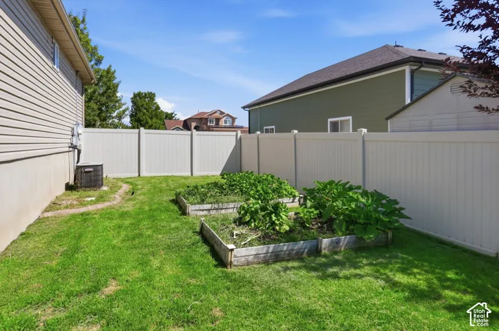 Fenced backyard oasis featuring a level, manicured lawn with raised garden beds, vinyl privacy fencing, and mature landscaping