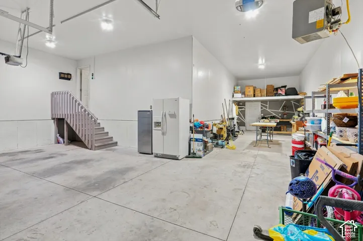Spacious garage featuring concrete flooring, a built-in staircase, an overhead storage loft and mounted garage heater