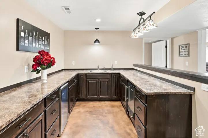 Galley-style bar featuring dark wood cabinetry with raised-panel doors, mini fridge, ice maker and sink