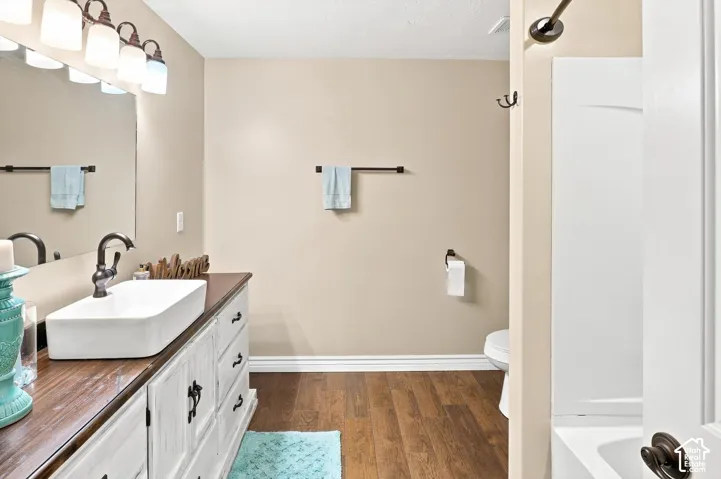 Spa-inspired primary bathroom featuring a vessel sink atop a wood-finish vanity with oil-rubbed bronze hardware, warm beige walls, wood-finish flooring, and a shower/tub combo