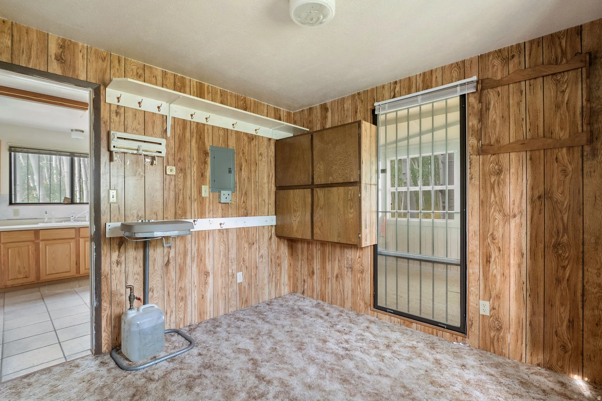 Room featuring wood paneling, a ceiling-mounted light fixture, direct access to the kitchen, bathroom and front entry area.