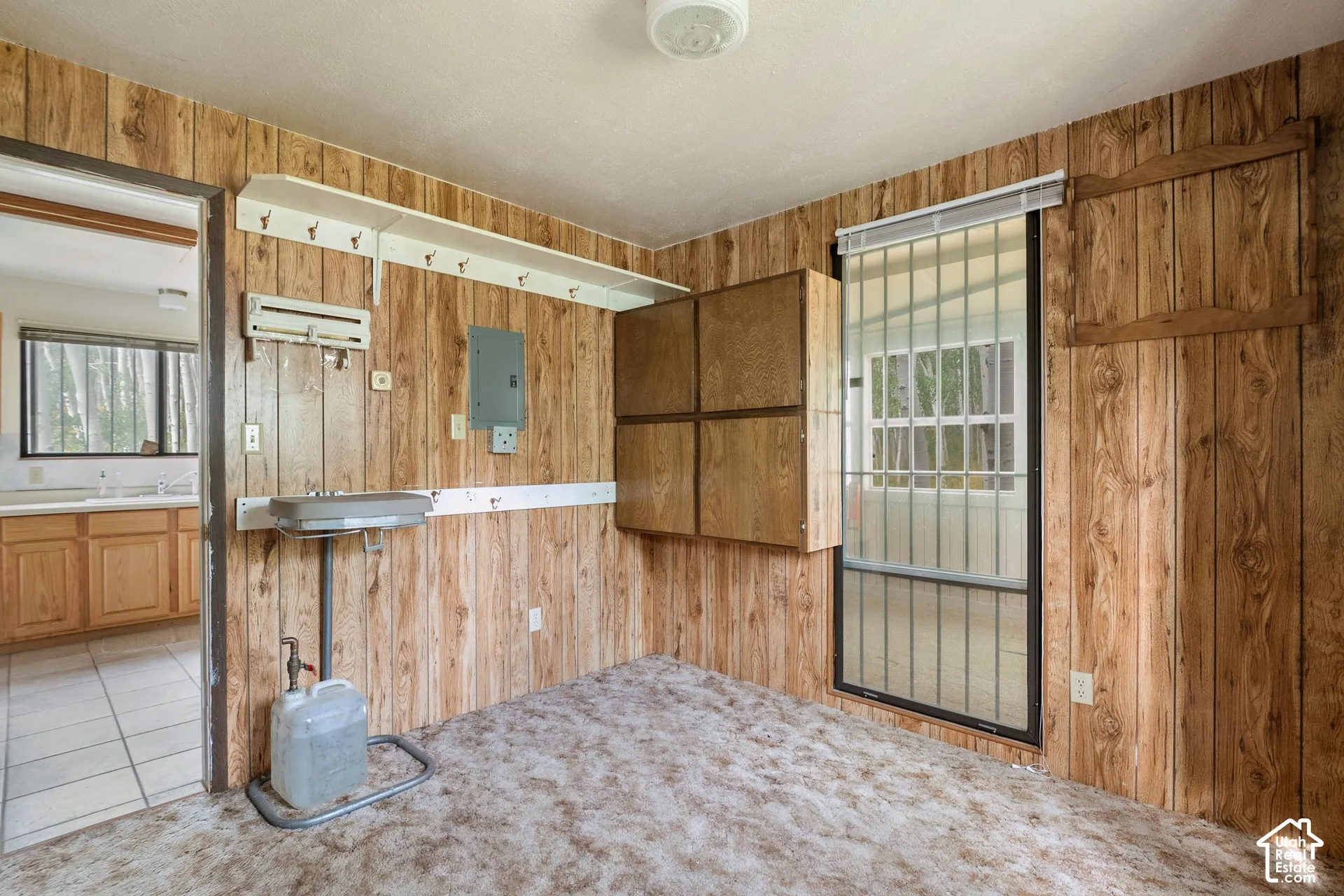 Room featuring wood paneling, a ceiling-mounted light fixture, direct access to the kitchen, bathroom and front entry area.