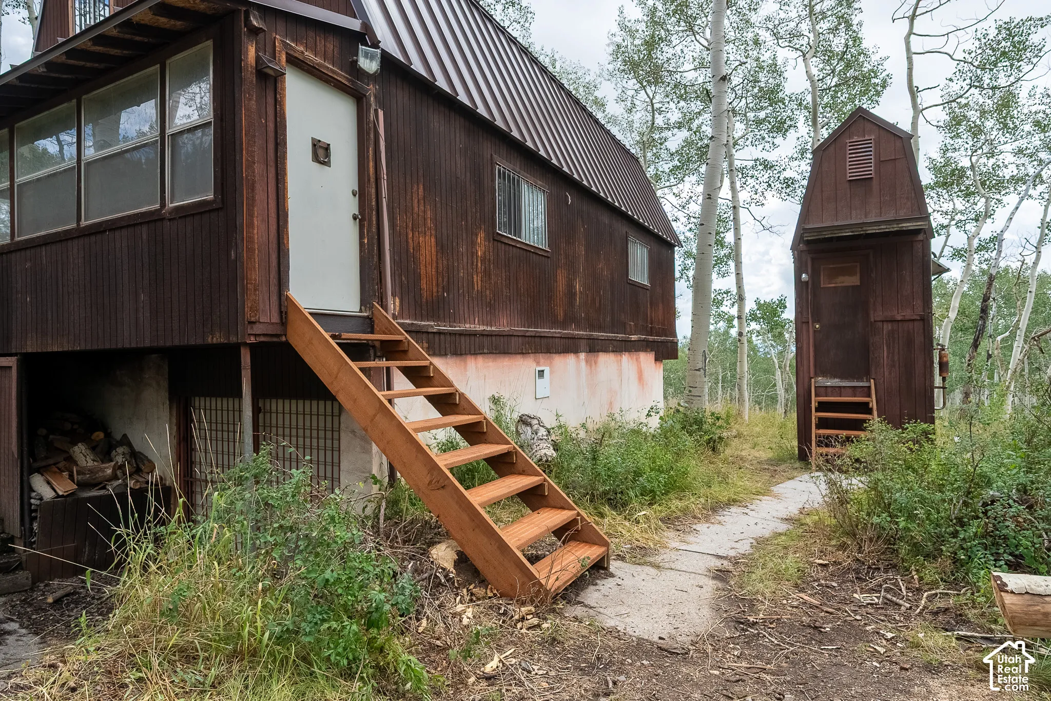Corrugated metal siding on the main structure, exterior stairs with natural wood finish, metal roof, detached shed with wood siding, mature deciduous trees