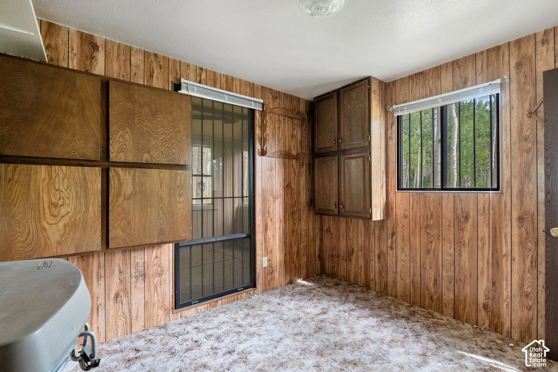 Room featuring wood-finish paneling, multiple integrated wood-finish cabinets, and a window with security bars