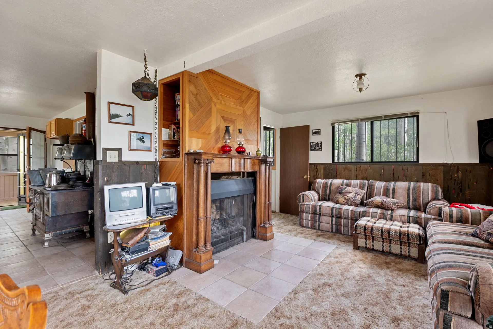 Living area featuring a prominent wood-clad fireplace surround with built-in shelving, wood-panel wainscoting, and large windows