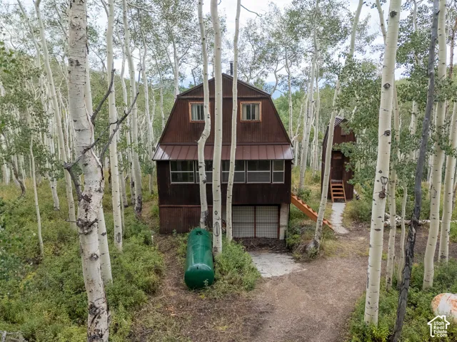 Corrugated metal siding exterior, gabled roofline, multiple windows, detached structure with exterior stairs, and extensive surrounding aspen trees