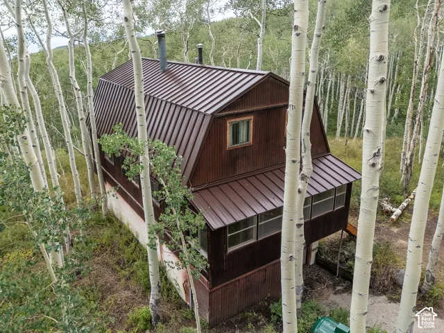 Gambrel roofline property featuring a brown metal roof, exterior wood siding, a covered porch, and mature surrounding trees