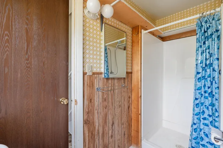 Full shower enclosure with white surround, wood-paneled walls, and patterned wallpaper