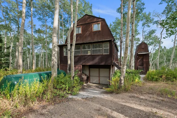Rustic multi-level dwelling featuring a corrugated metal exterior, surrounded by tall aspen trees