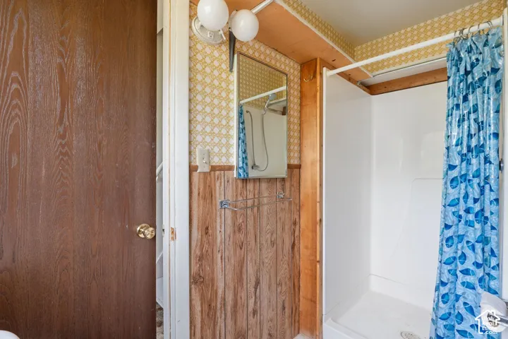 Full shower enclosure with white surround, wood-paneled walls, and patterned wallpaper