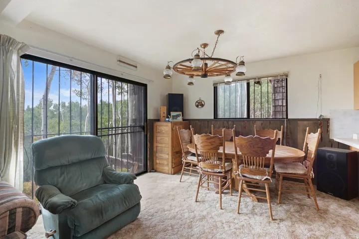 Spacious room featuring wood-finish paneling, a large sliding glass door with exterior security bars, and a wood wagon wheel chandelier