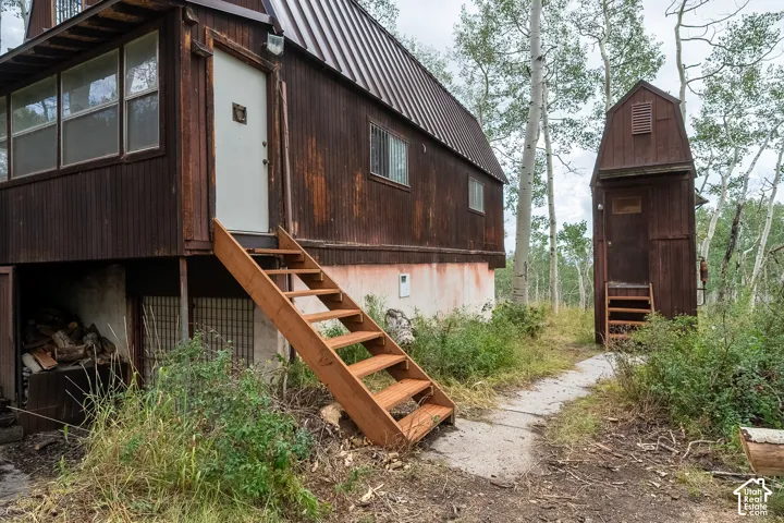 Corrugated metal siding on the main structure, exterior stairs with natural wood finish, metal roof, detached shed with wood siding, mature deciduous trees