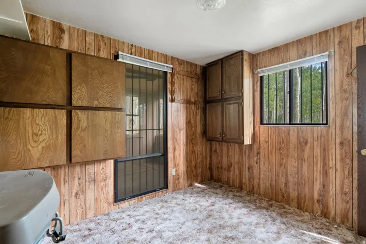 Room featuring wood-finish paneling, multiple integrated wood-finish cabinets, and a window with security bars